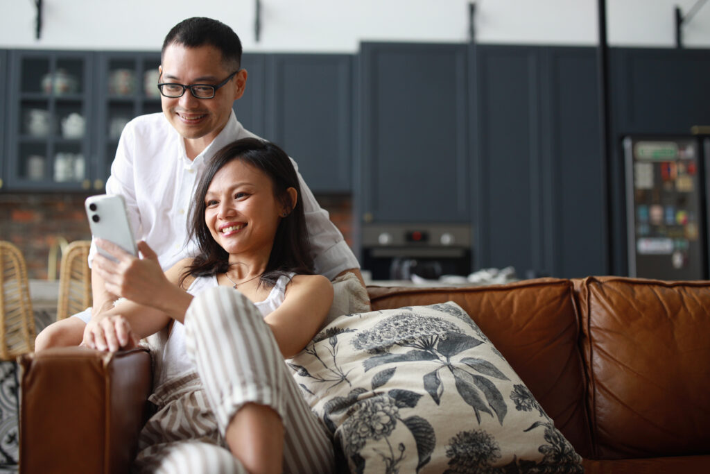 Couple sitting on couch viewing smartphone together for continuous healthcare support