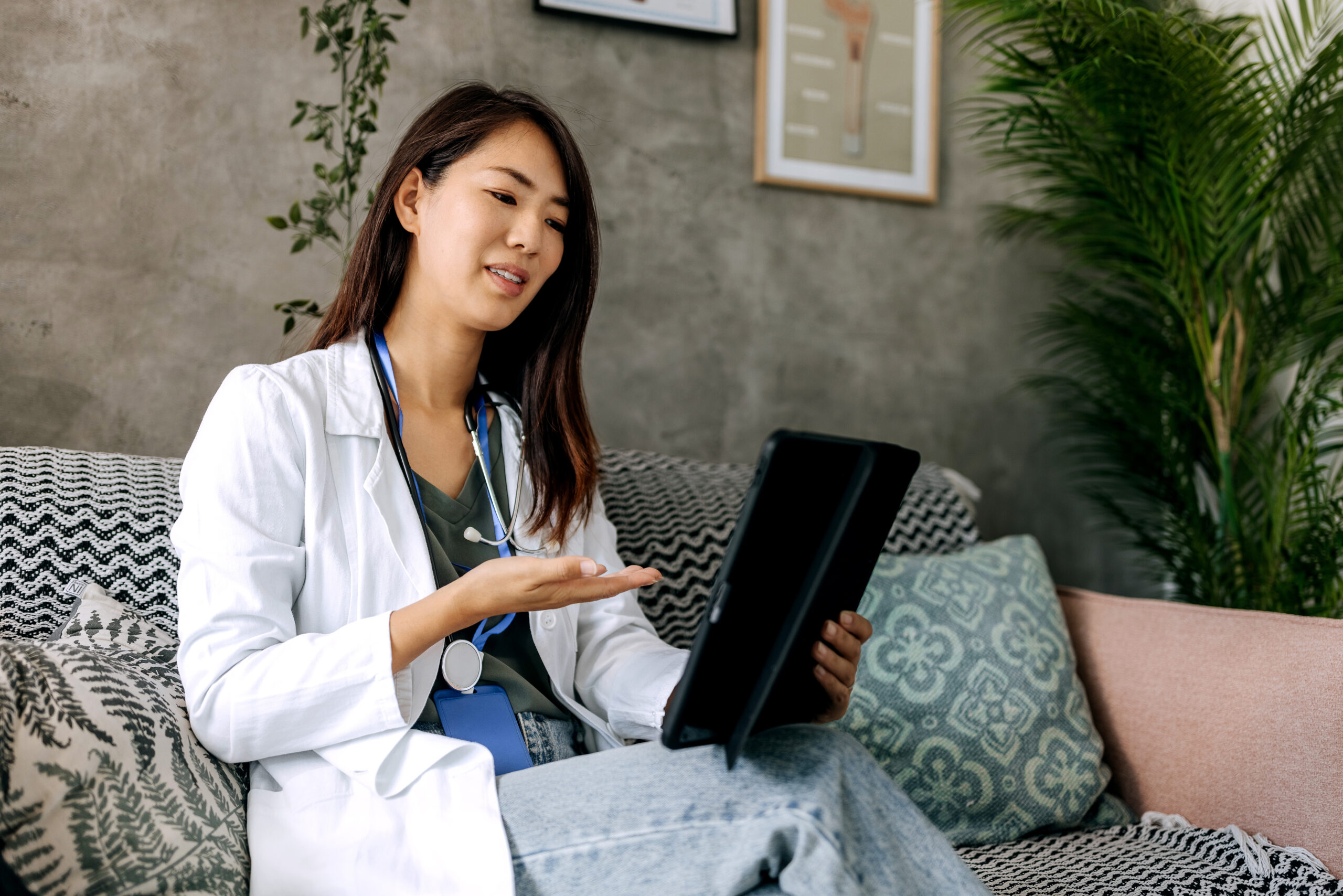 Female doctor on sofa with tablet providing healthcare follow-up consultation virtually