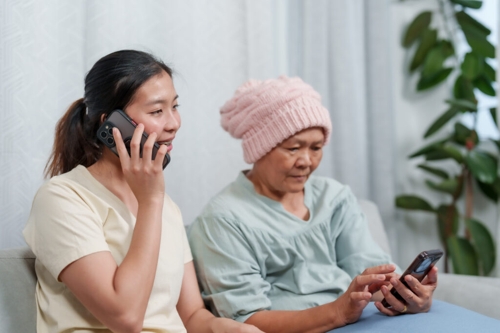 Wanita warga emas duduk di atas katil hospital sementara anak perempuannya bercakap melalui telefon mengenai insurans kesihatan