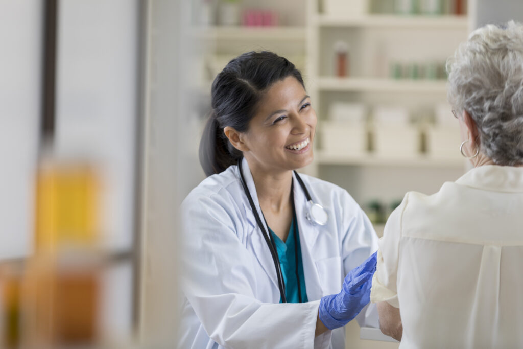 Female doctor smiling while holding an elderly woman’s hand talking about AI healthcare