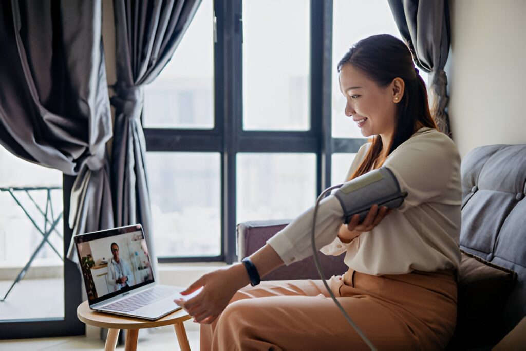 A woman monitoring her high blood pressure at home using a digital cuff during a video call with a doctor