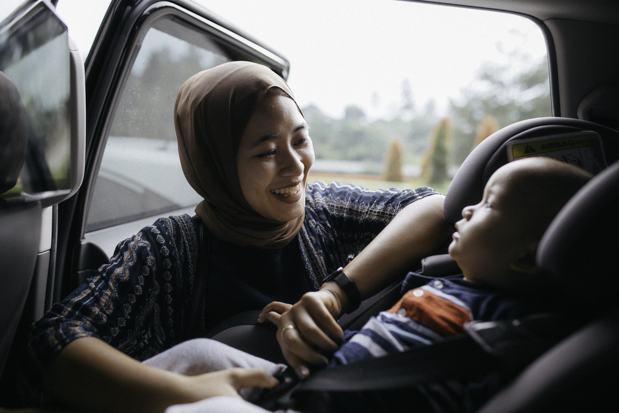 Smiling woman fastening a baby into a car seat following telemedicine guidance for safe family travel