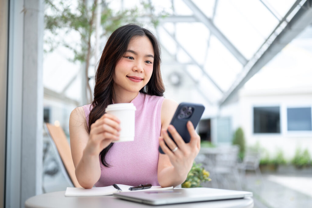 Woman sipping coffee and browsing her phone, thinking about affordable healthcare Malaysia