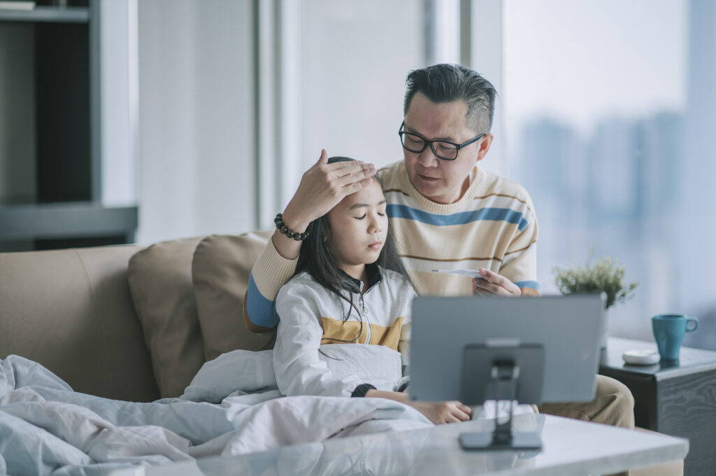 Father checking his sick daughter's fever as part of family healthcare